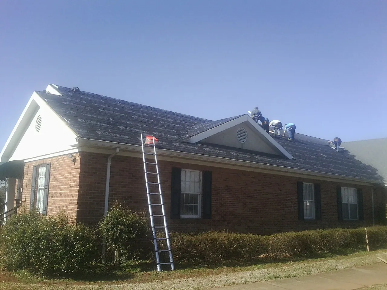 Crew tearing shingles off a brick ranch roof with a ladder set — Emergency Roof Repair work by our crew in Rutherfordton