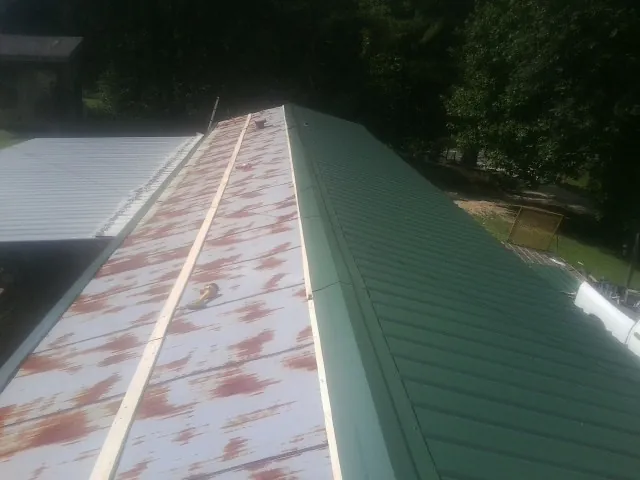 Old rusted panels beside newly installed green metal roofing — Wind Damage Roof Repair by Roofing Brothers in Rutherfordton
