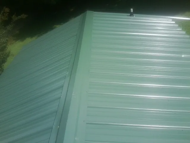 New green metal panels meeting at the ridge of a roof — Flat Roof Repair work by our crew in Rutherfordton