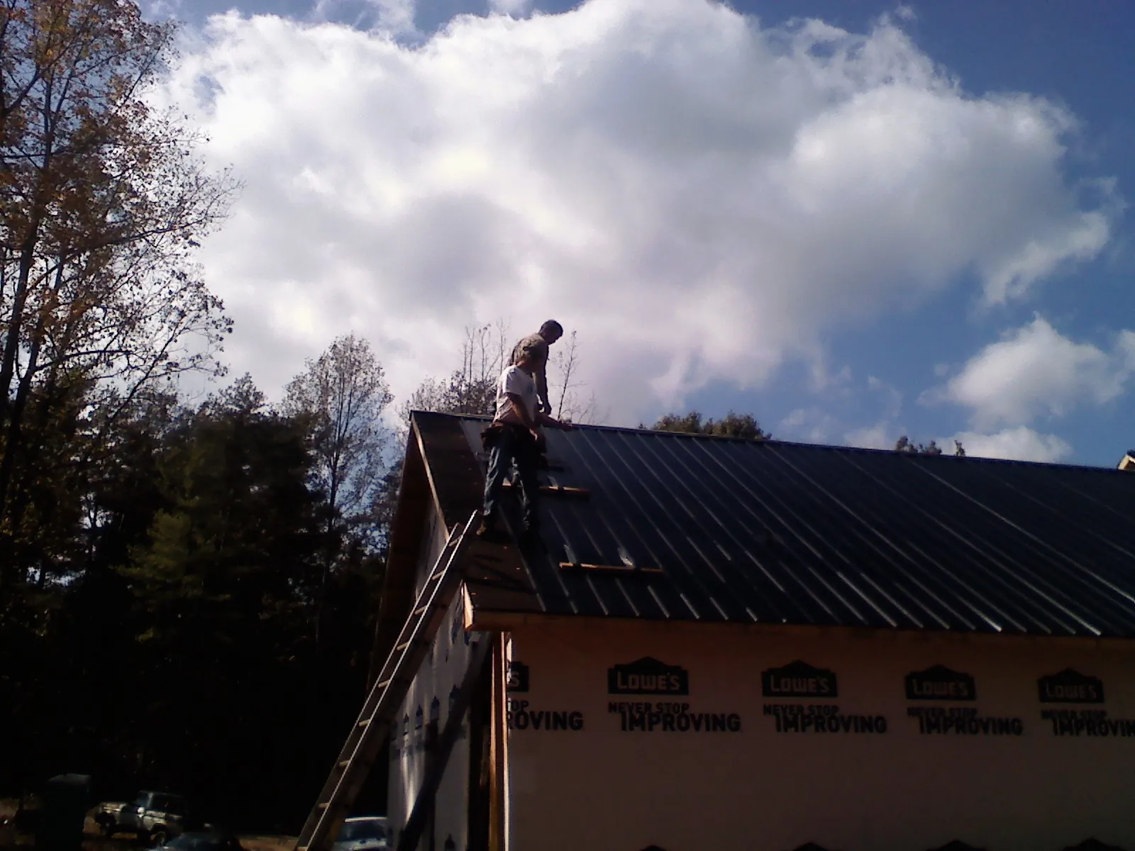 Roofer fastening dark metal panels high against a cloudy sky, from a Roof Inspection job in Rutherfordton
