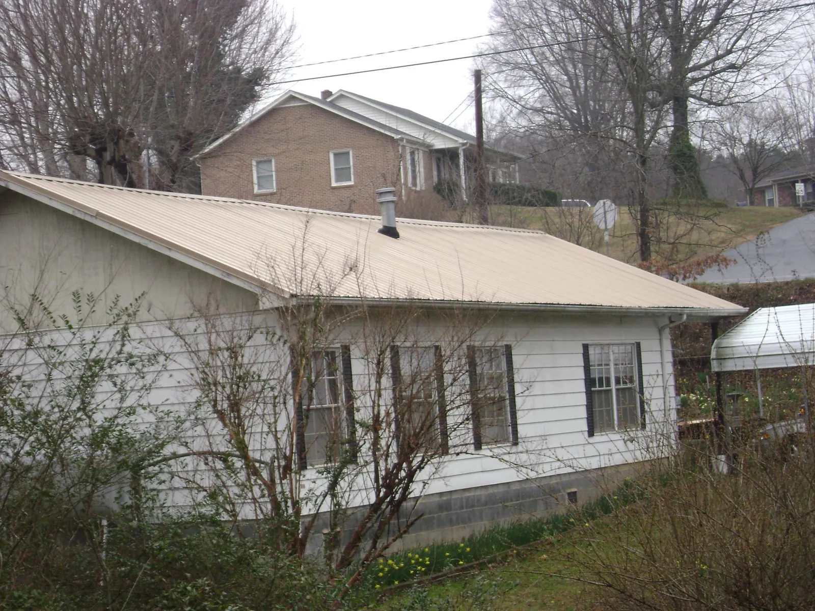Tan metal roof on a white sided house set into a hillside — Commercial Roofing by Roofing Brothers in Rutherfordton
